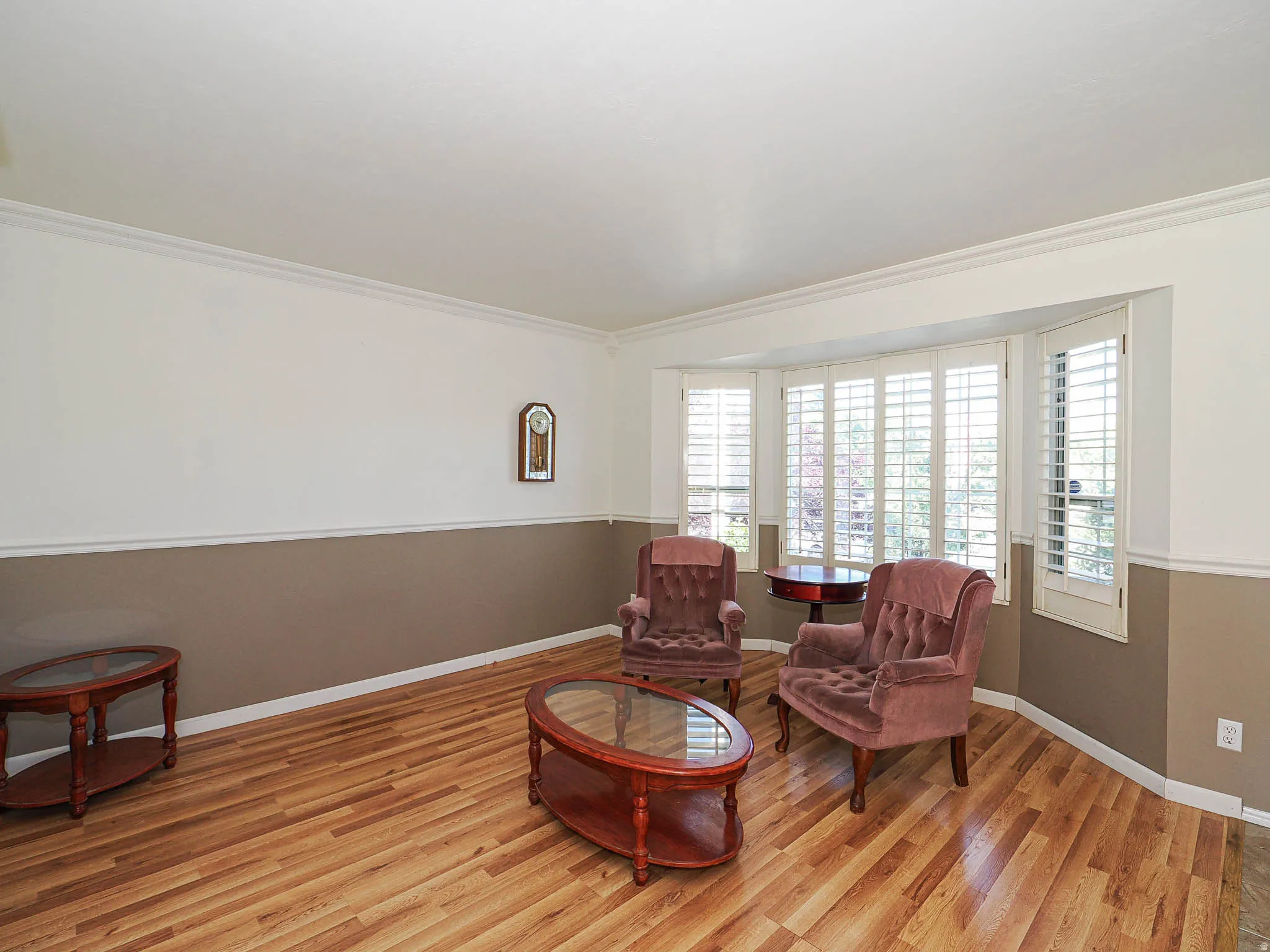 Spacious interior featuring wood-finish flooring, two-tone wall paint, and a bay window with plantation shutters