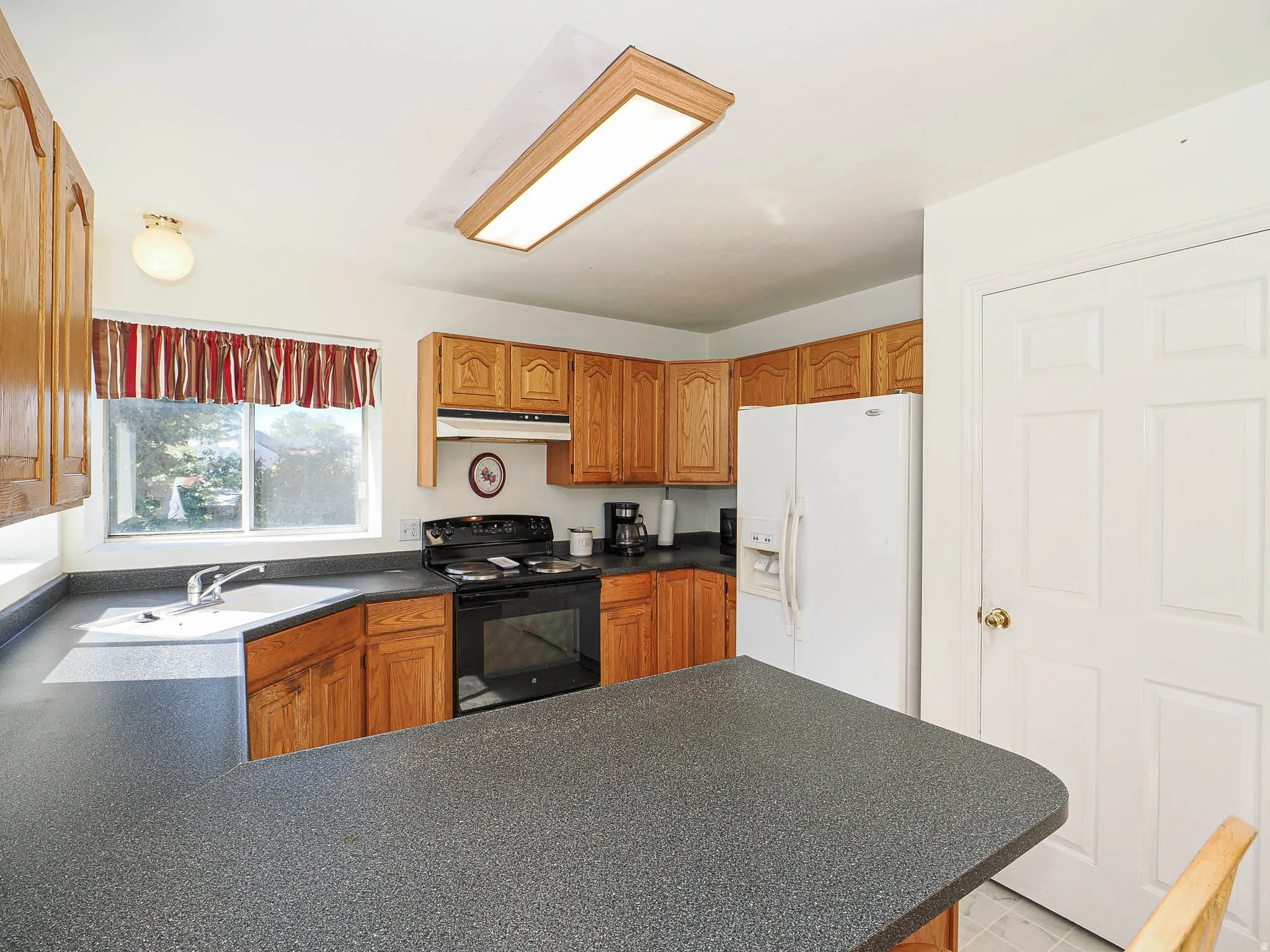 Kitchen featuring wood cabinetry, dark countertops, a built-in corner sink, a black range, and white appliances