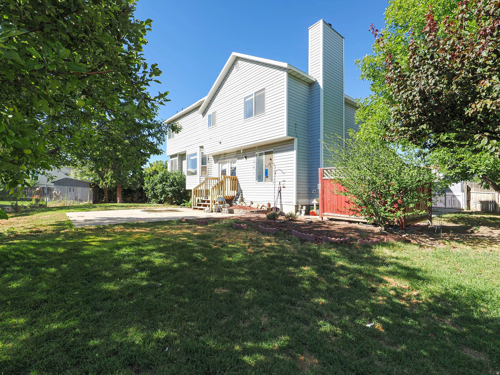 Expansive lawn area with a concrete patio, mature trees, and a multi-level wooden deck