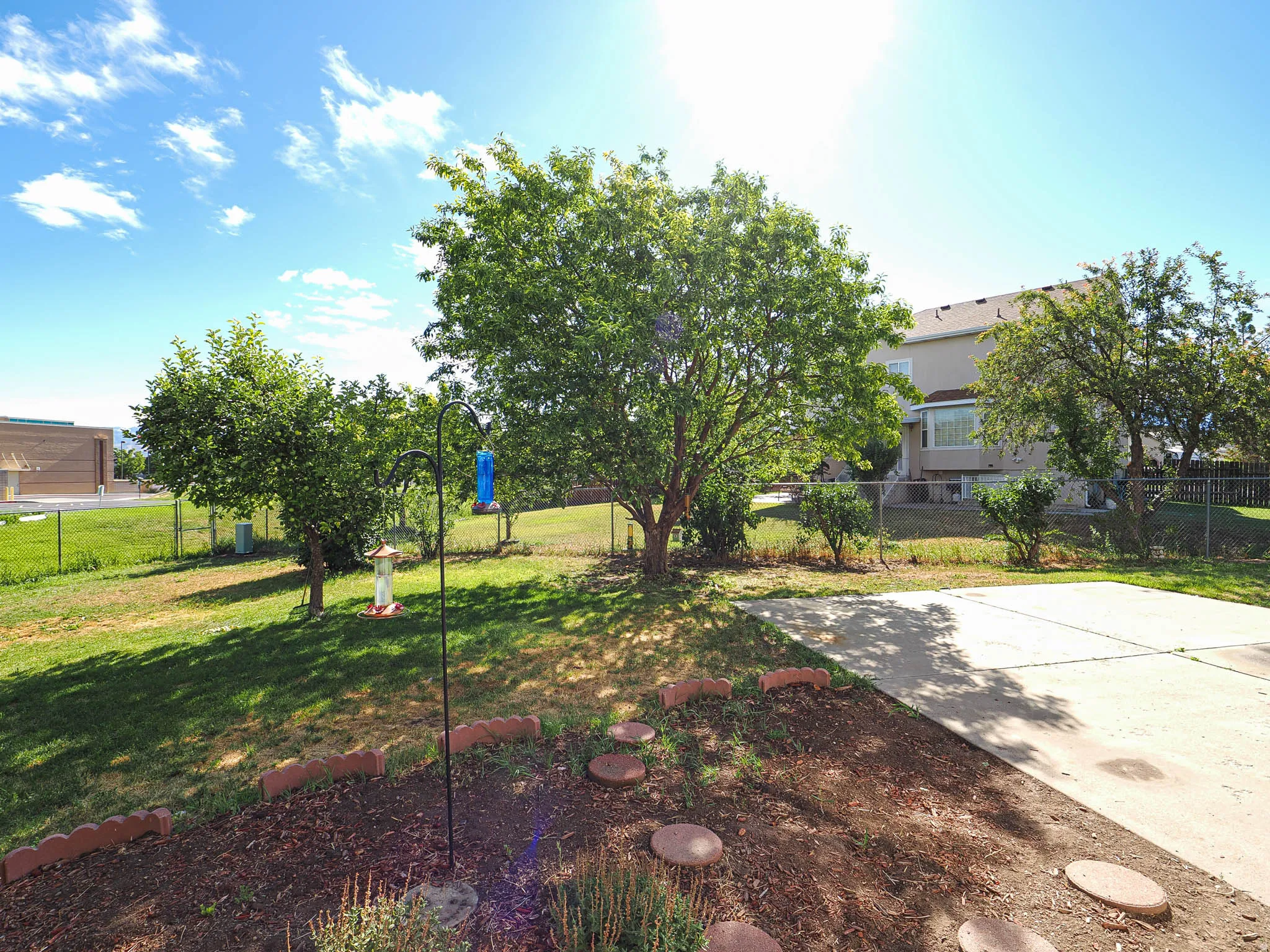 Expansive backyard featuring mature trees, a concrete patio area, and a chain-link fence defining the property perimeter