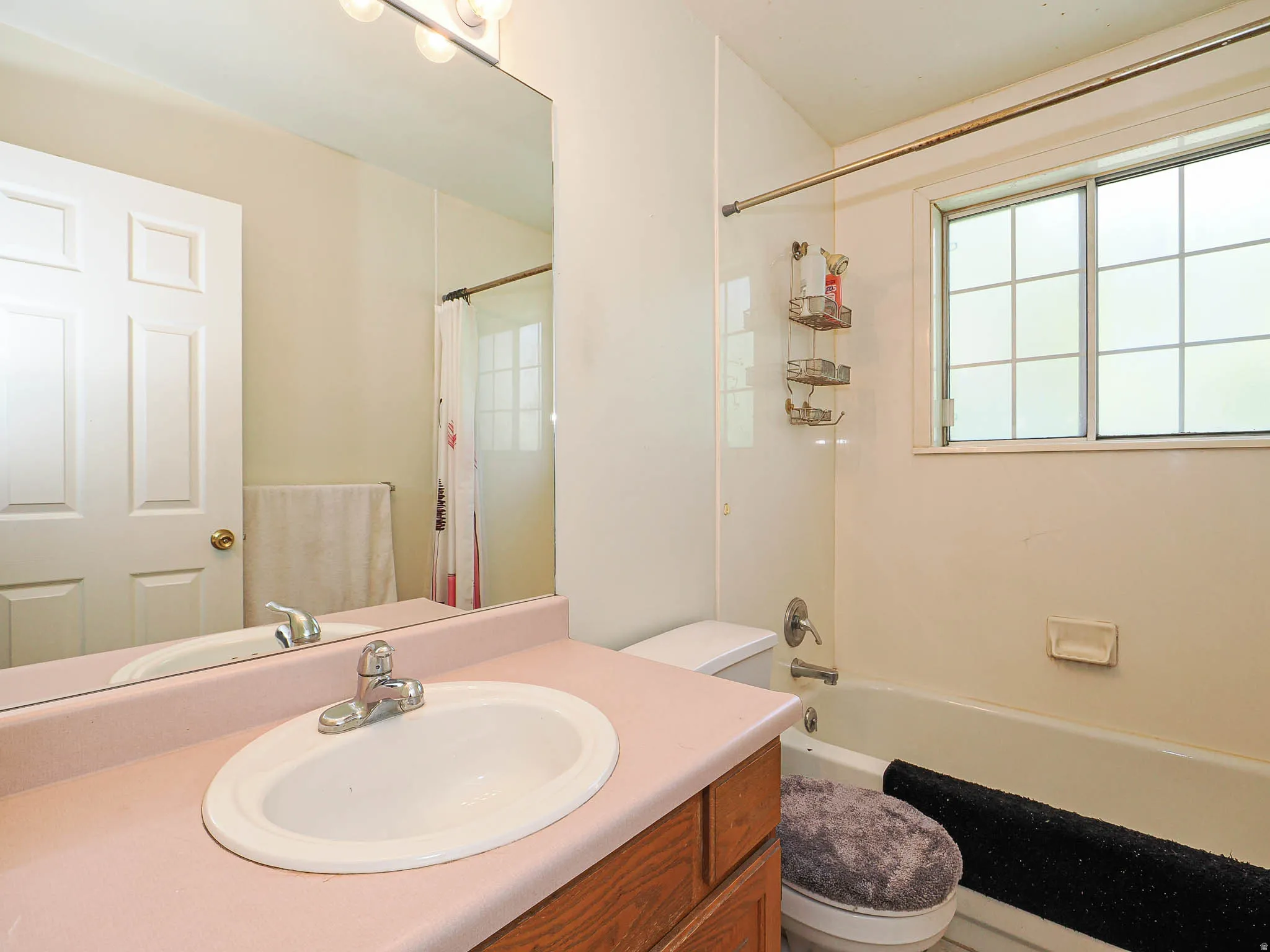 Full bathroom featuring a single vanity with an integrated sink, a large wall-mounted mirror, overhead vanity lighting, and a combination shower/bathtub with a window