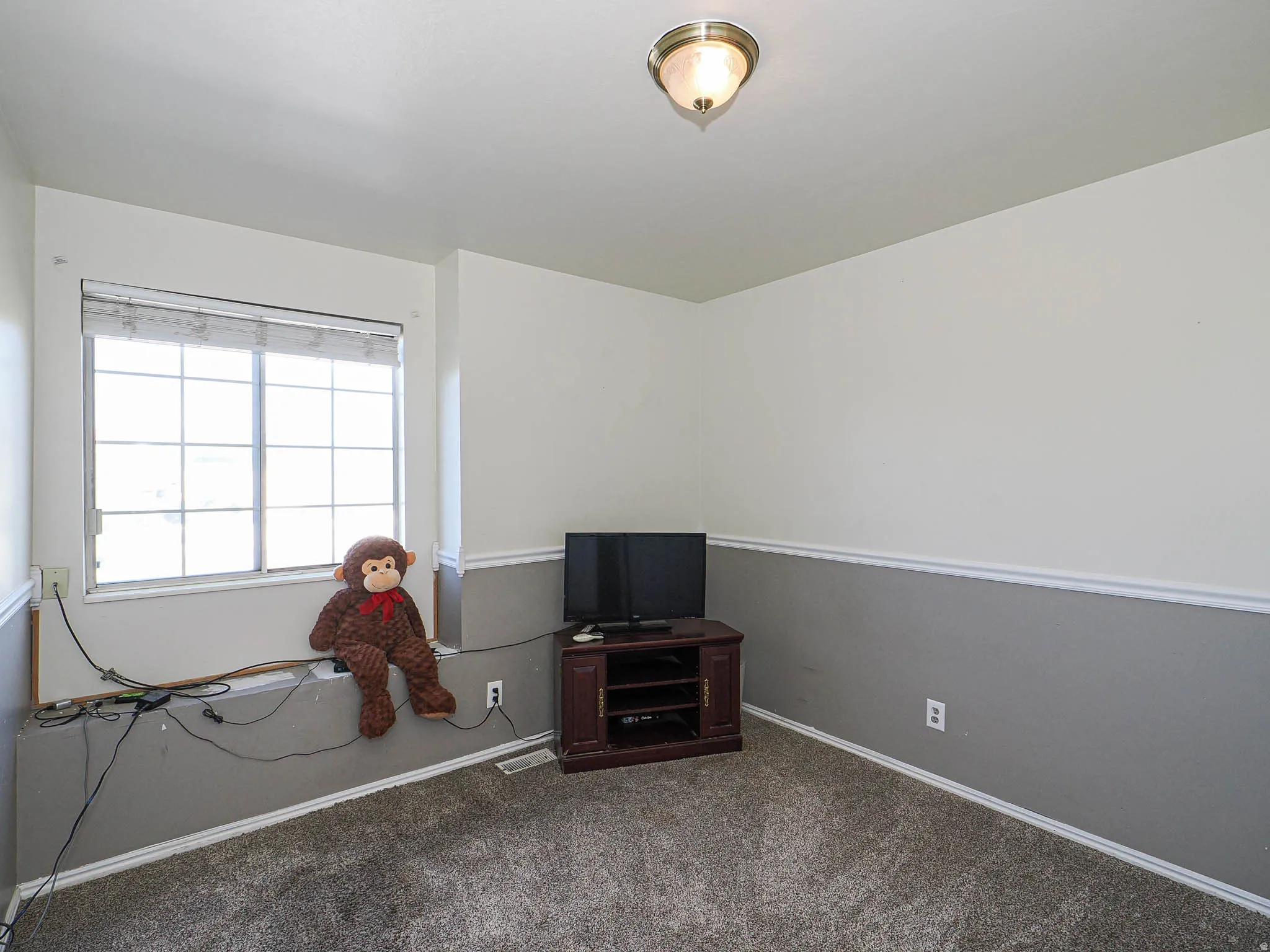 Carpeted room with a multi-pane window, two-tone wall treatment with chair rail molding, and a flush-mount ceiling light fixture
