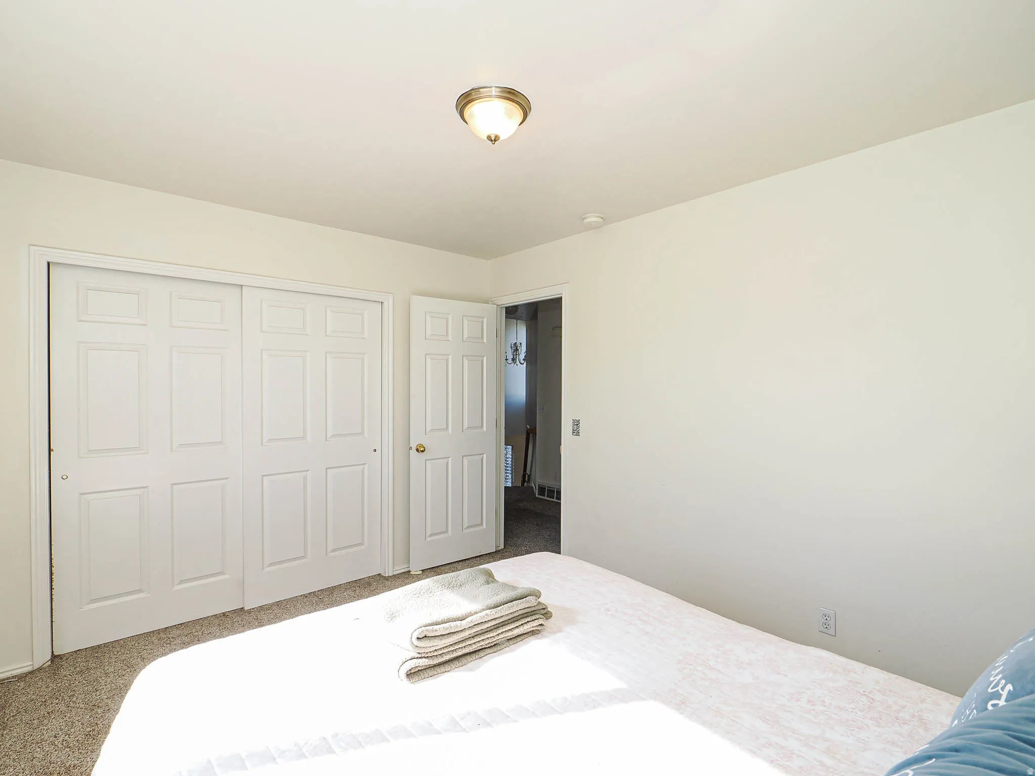 Bedroom featuring light neutral wall paint, carpet flooring, a flush-mount ceiling light fixture, and white bi-fold closet doors