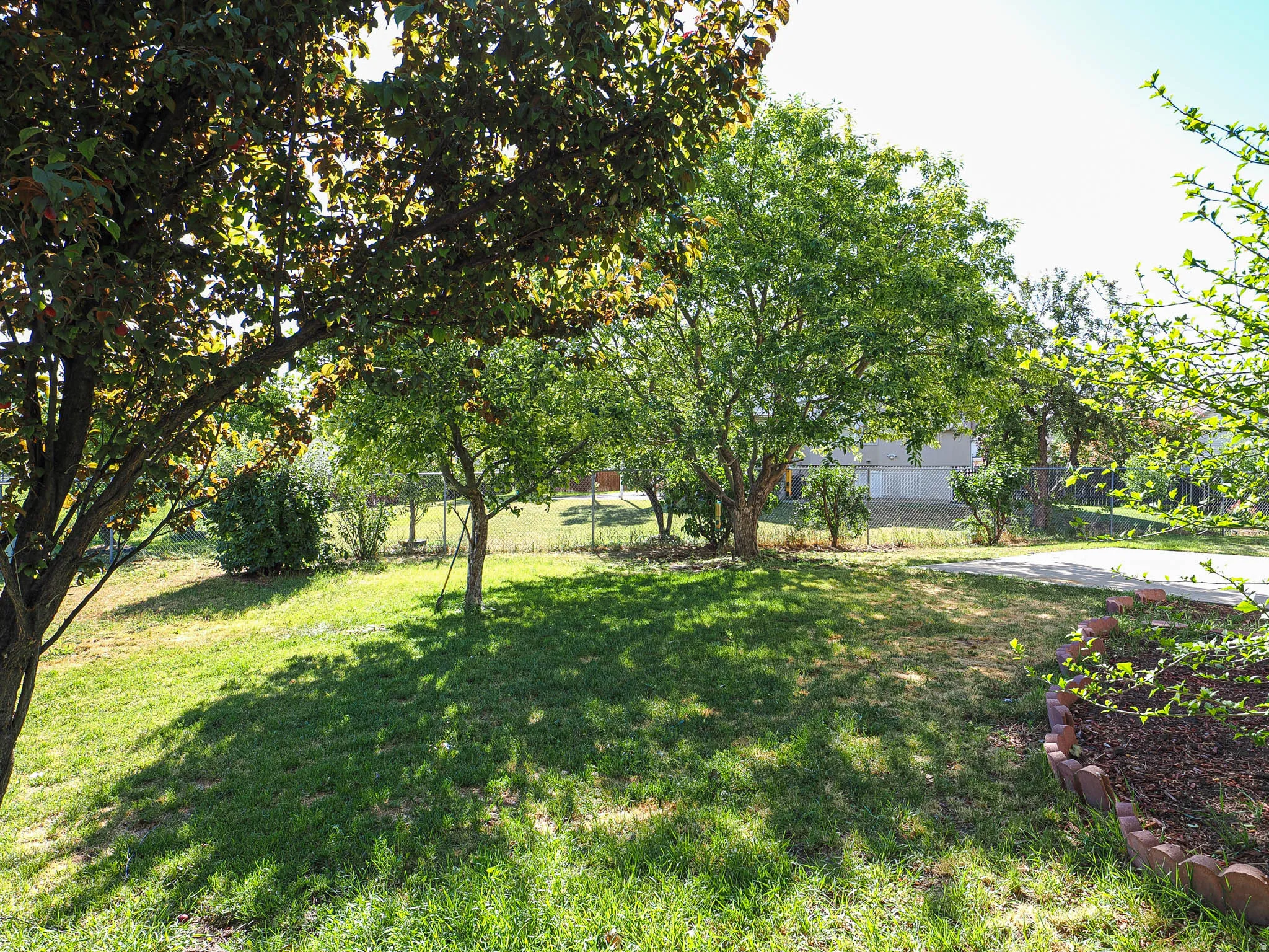 Expansive lawn featuring mature shade trees, a garden bed with brick edging, and a paved path