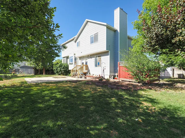 Expansive lawn area with a concrete patio, mature trees, and a multi-level wooden deck