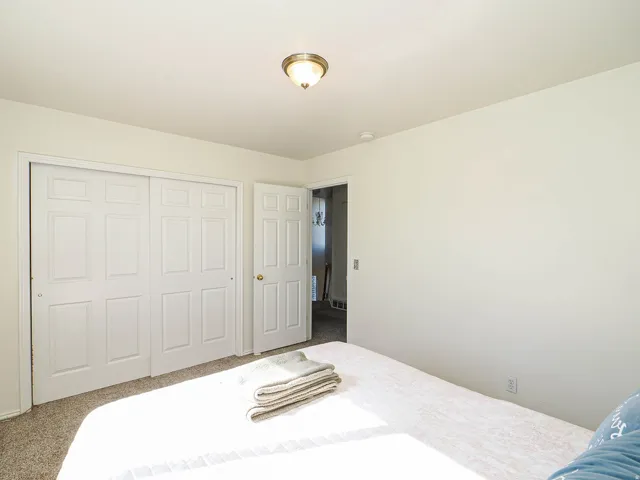 Bedroom featuring light neutral wall paint, carpet flooring, a flush-mount ceiling light fixture, and white bi-fold closet doors