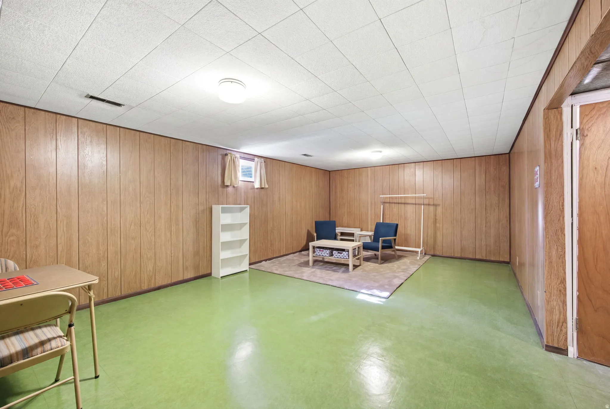 Finished basement space featuring wood-panel walls, a green-toned floor, and a white ceiling with recessed lighting