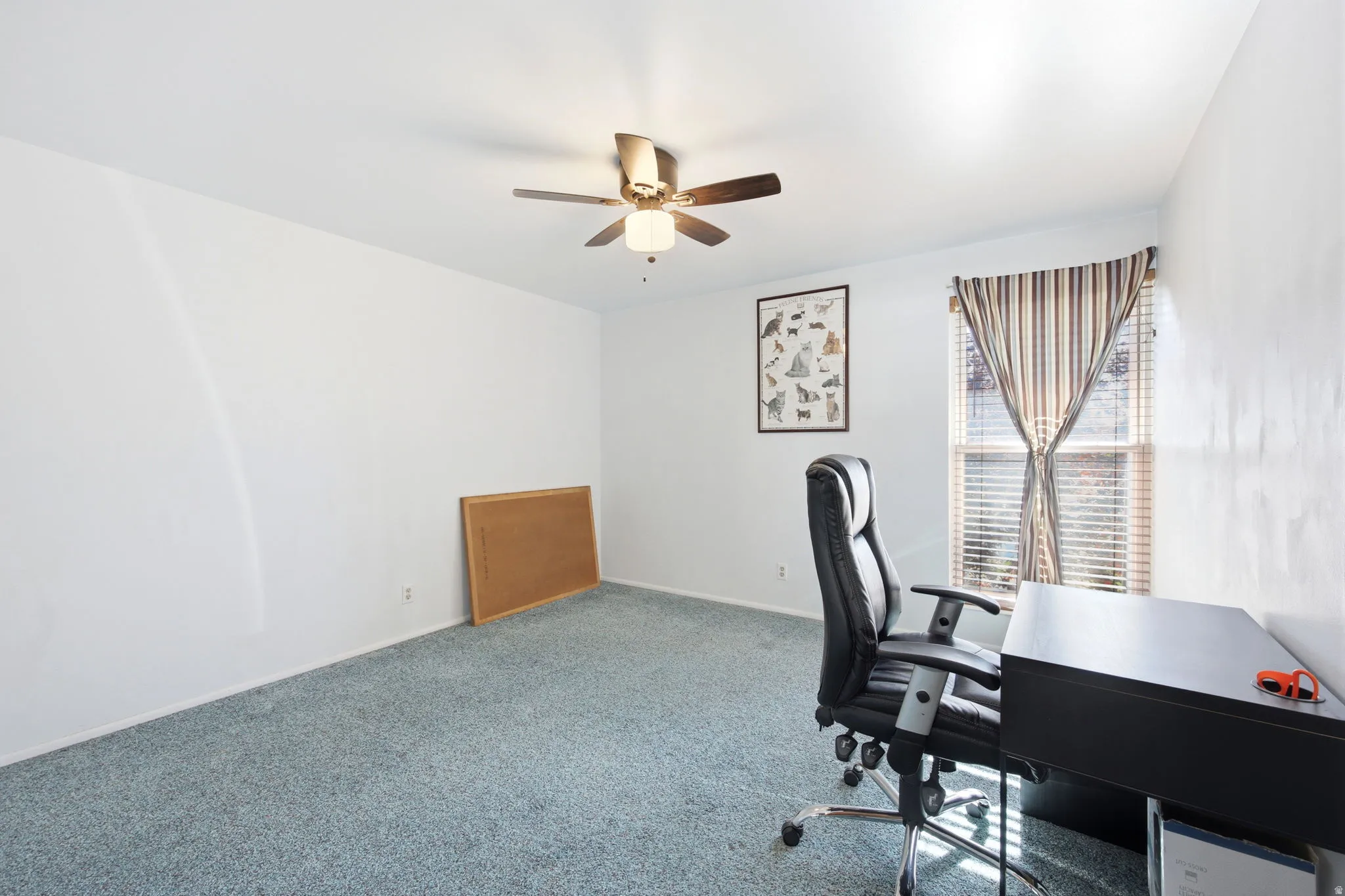 Carpeted room with a ceiling fan, white walls, and a window featuring blinds and striped valance