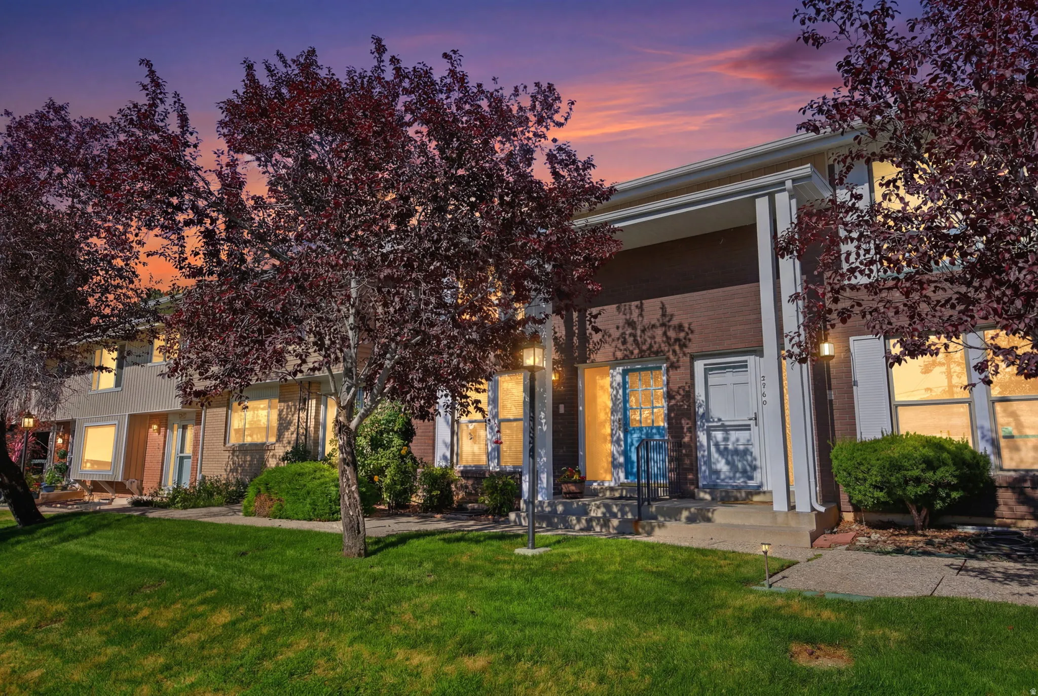 Townhome exterior featuring brick and siding finishes, mature landscaping, and an inviting front entry with a contrasting door