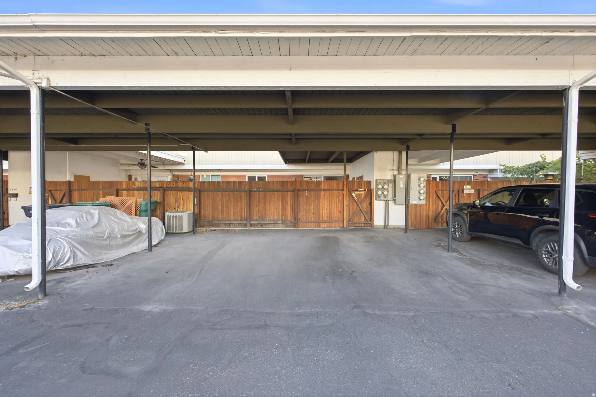 Covered parking structure featuring multiple bays, a composite shingle roof, painted white fascia, and a wood fence perimeter