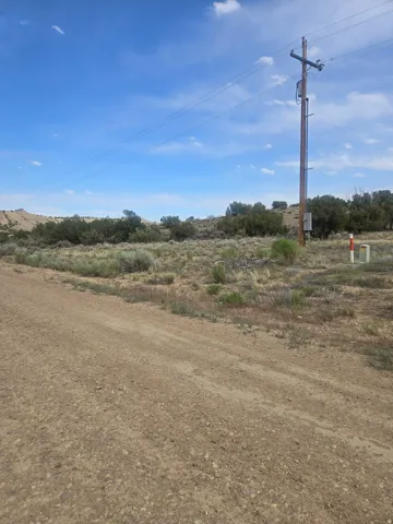 Expansive undeveloped land featuring natural desert vegetation, a utility pole with overhead lines, and a gravel road
