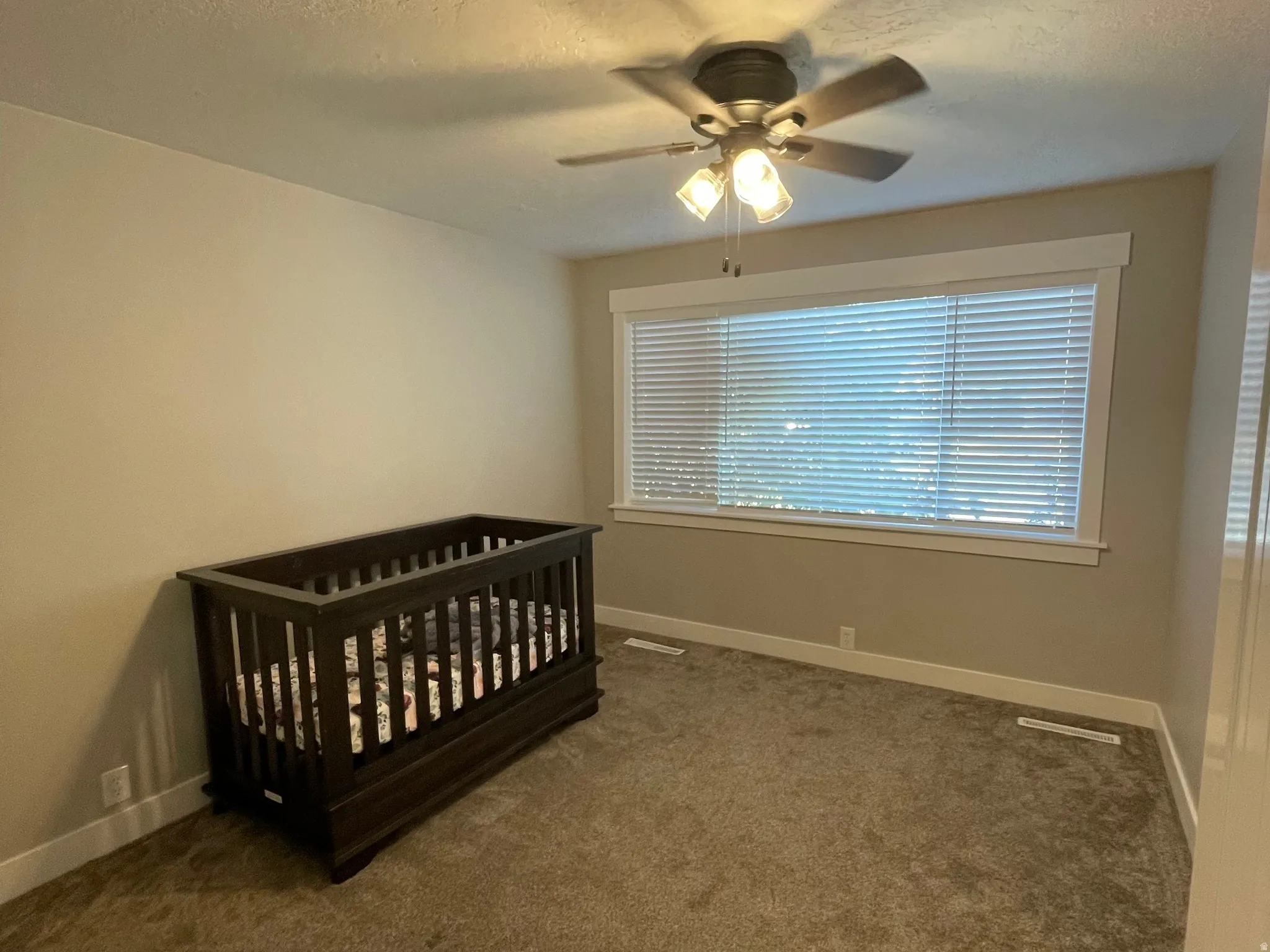 Carpeted room featuring a ceiling fan with integrated lighting, a wide window with blinds, and white trim