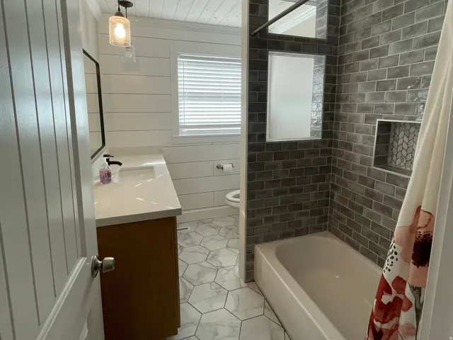 Bathroom featuring a vanity with an integrated sink and matte black faucet, shiplap walls, a tub/shower combination with subway tile surround, and hexagonal floor tiling