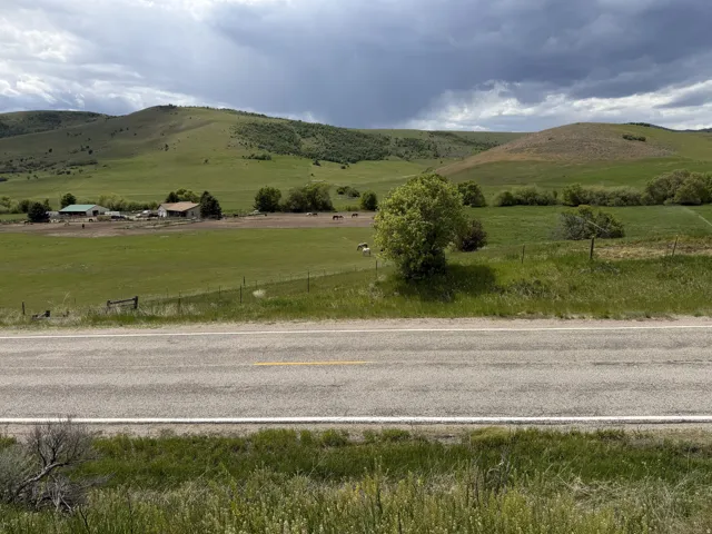 Expansive green pastures framed by rolling hills, featuring multiple structures including a dwelling with a light-colored roof and a barn with a green roof