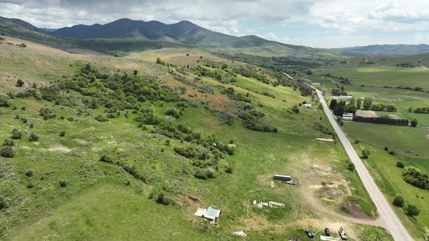 Expansive parcel featuring a paved road frontage, verdant hillsides, distant mountain range, and scattered mature trees