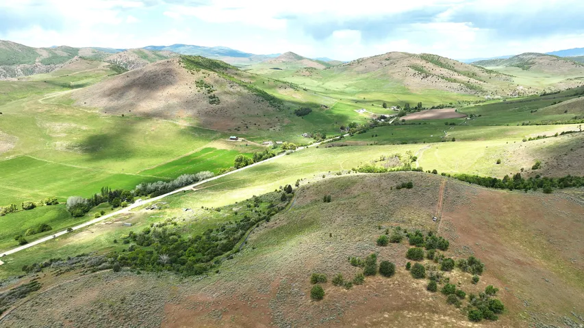 Expansive terrain featuring rolling hills, varied green and brown vegetation, and distant structures