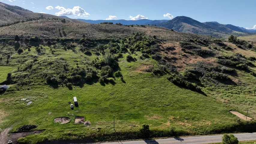 Expansive parcel featuring a verdant grassy field, rolling hills with varied foliage, and a paved road bordering the property