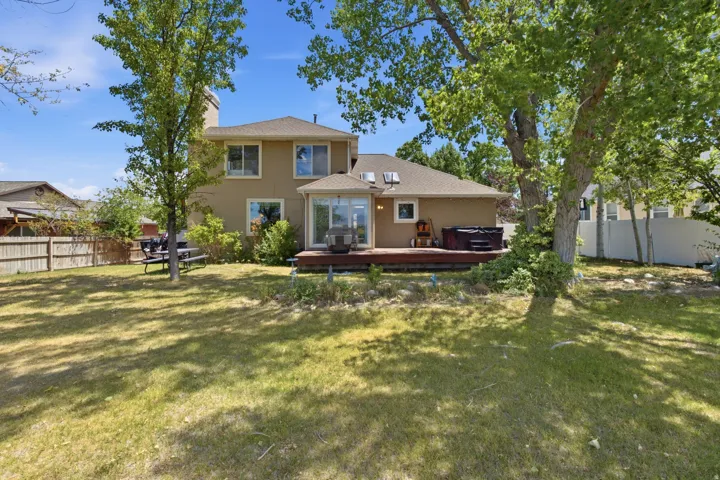 Spacious rear yard with a two-story stucco exterior, a large wooden deck, multiple mature trees, and a ground-level patio space