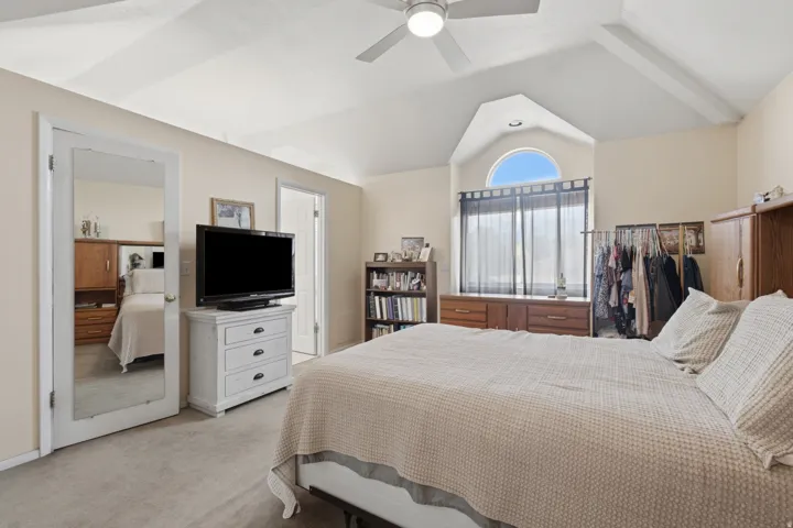 Vaulted ceiling bedroom featuring a ceiling fan, arched window, carpeted flooring, and a mirrored door