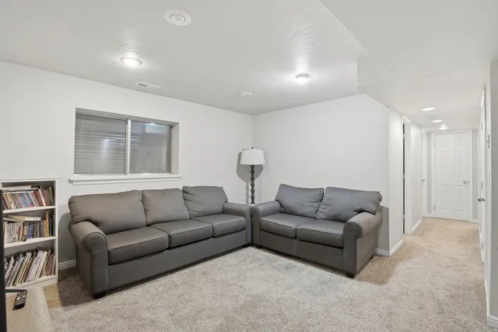 Carpeted recreation room featuring white walls, recessed lighting, and a single window with blinds