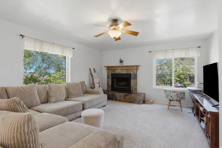 Living area featuring a stone-clad fireplace with a wood mantle, a ceiling fan with integrated lighting, and carpeted flooring