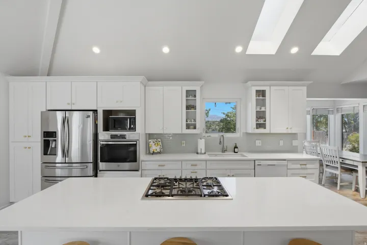 Spacious kitchen featuring white cabinetry, stainless steel appliances, a center island with a built-in gas cooktop, and a tile backsplash