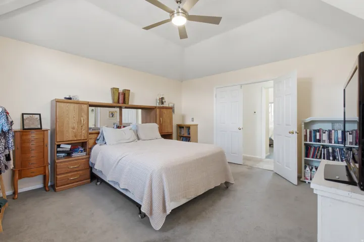 Vaulted ceiling bedroom featuring carpeting, a ceiling fan, light-toned wall paint, and white paneled doors