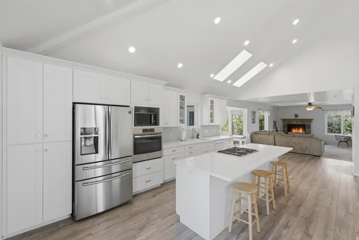 Modern kitchen featuring white cabinetry, stainless steel appliances, a center island with a cooktop, and wood-finish flooring