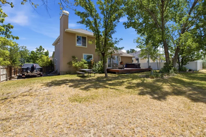 Expansive backyard featuring a multi-level wooden deck, mature trees providing shade, and a hot tub