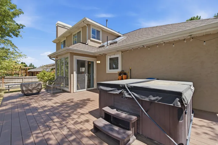 Expansive composite deck featuring a built-in hot tub with steps, string lighting, and a sunroom with large glass windows and a sliding glass door