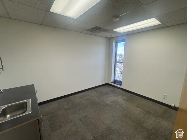 Interior room featuring a single window, drop ceiling with fluorescent lighting, and modular carpet flooring