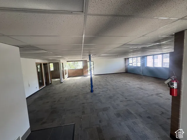 Expansive open-concept room featuring modular carpet flooring and a suspended acoustic tile ceiling