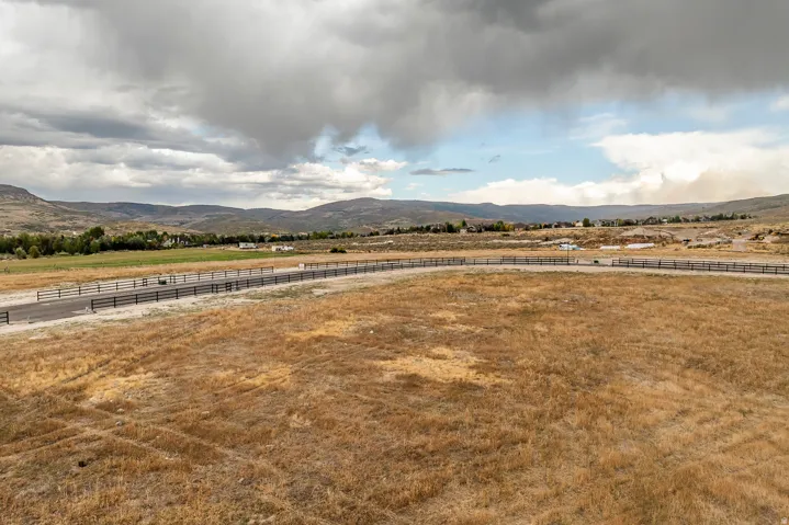 Expansive land parcel featuring a paved road, mountain backdrop, and distant residential structures