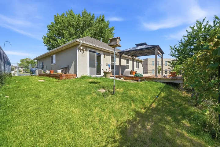 Rear exterior featuring a spacious wood deck, dedicated gazebo structure, sliding glass door access, and a sloped grass yard