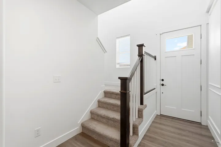 Entryway featuring wood-finish flooring, a white paneled door with transom window, a carpeted staircase with dark wood newel posts and handrail, and white vertical balusters