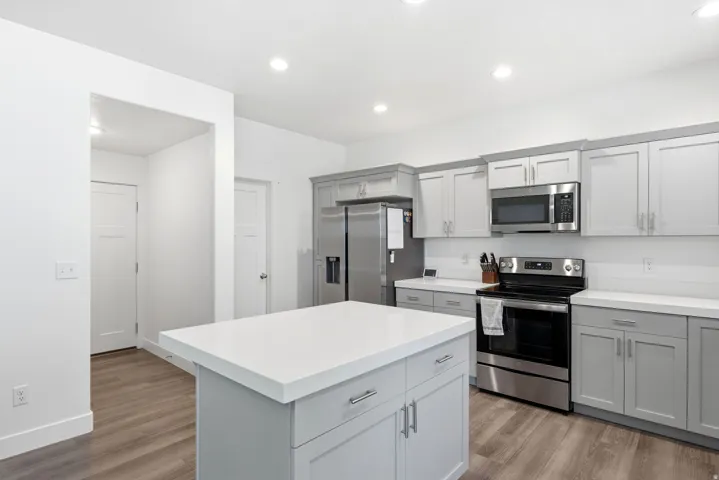 Kitchen featuring a center island with a white countertop, coordinating gray cabinetry, stainless steel appliances, and wood-finish flooring