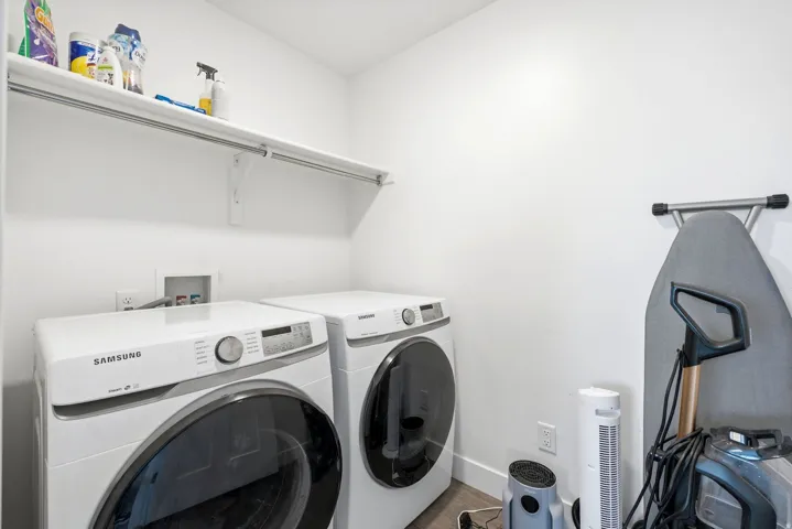 Dedicated laundry area featuring a white wall shelf with a clothing rod, two front-loading appliances, and wood-finish flooring