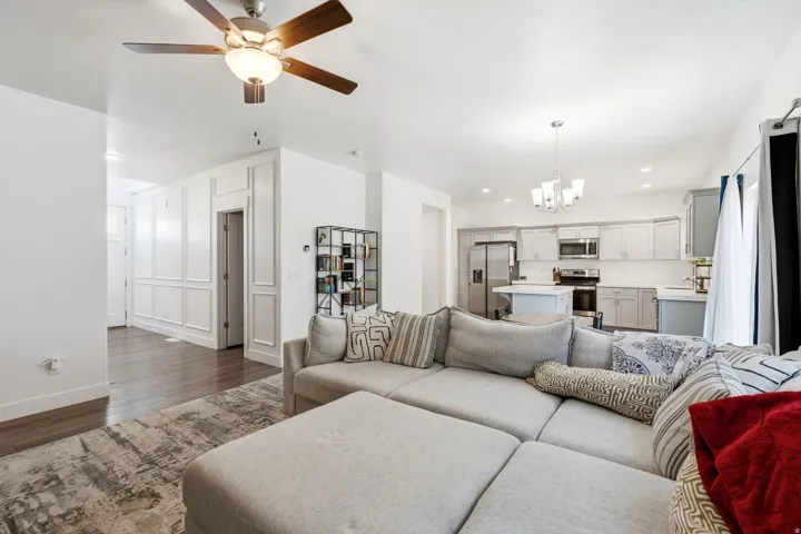 Open-concept living area with wood-finish flooring, white paneled wall accents, a modern ceiling fan, and a kitchen featuring stainless steel appliances and light-toned cabinetry