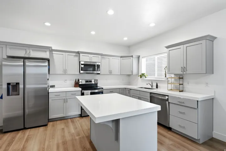 Modern kitchen featuring light gray shaker cabinetry, white countertops, wood-finish flooring, stainless steel appliances, and a central island