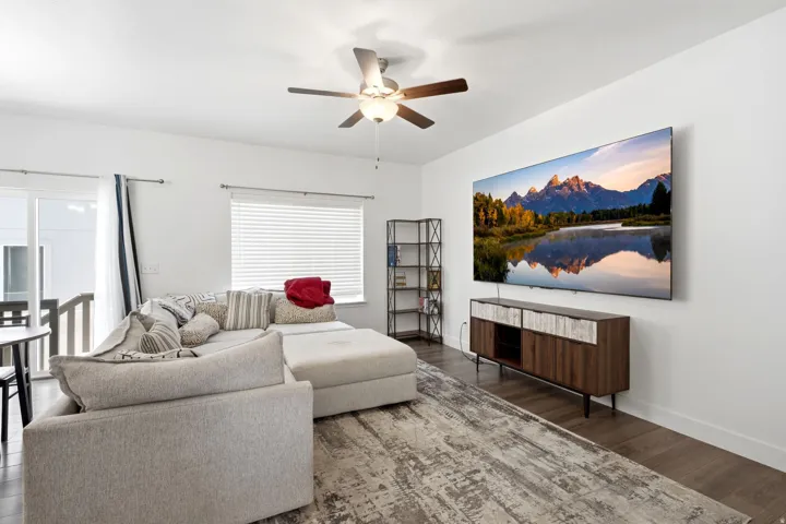 Spacious living area featuring wood-finish flooring, a ceiling fan with integrated lighting, and a large sliding glass door opening to an exterior deck