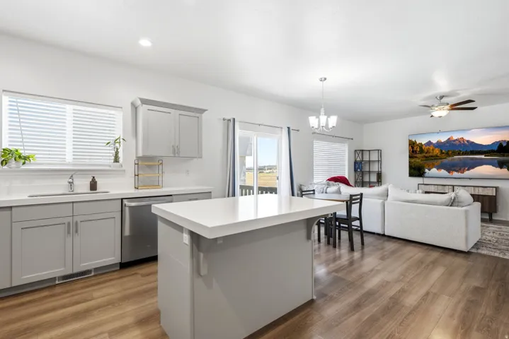 Open-concept living space with wood-finish flooring, featuring a kitchen island with a light-toned countertop, gray cabinetry, and stainless steel appliances