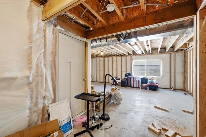Unfinished basement with exposed ceiling joists and framing, offering a concrete floor, a window, and a white interior door