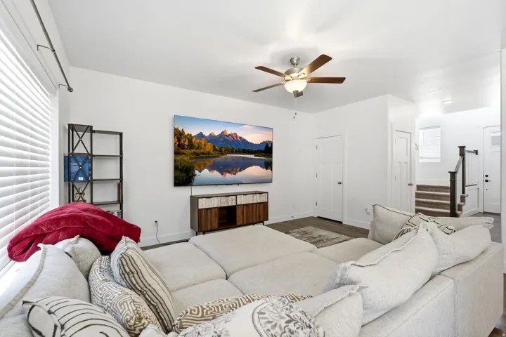 Living area featuring a ceiling fan with integrated lighting, a wall-mounted entertainment display, and wood-finish flooring
