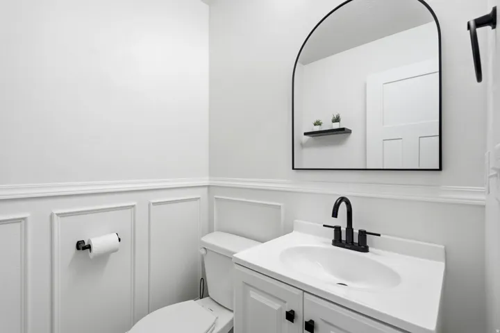 Modern vanity with integrated sink, black hardware, arched mirror, and wainscoting
