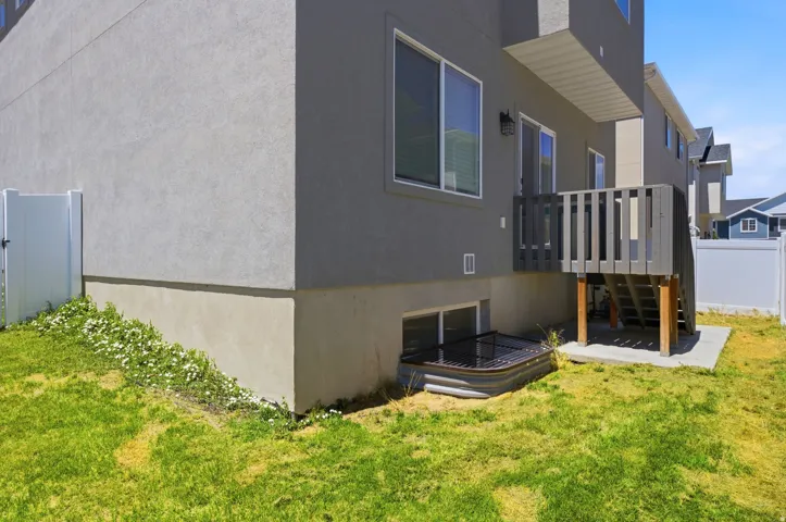 Rear exterior featuring a grey stucco finish, ground-level window well, and an upper-level  Trex deck with vertical railing