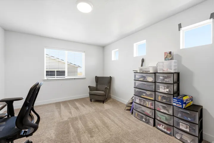 Carpeted interior space with neutral wall tones, featuring a large window with horizontal blinds and multiple high-set windows