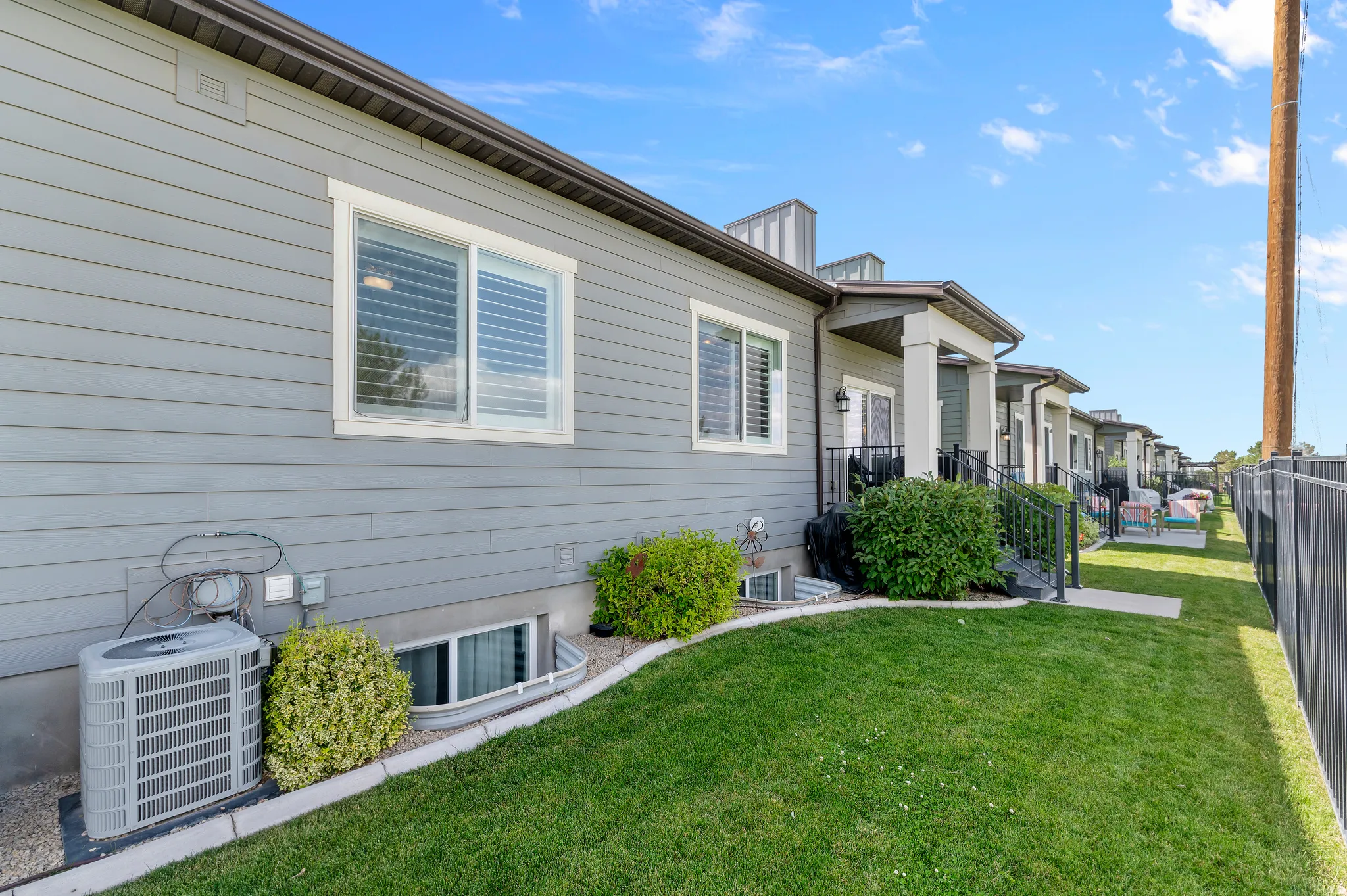 HOME EXTERIOR - REAR Manicured lawn extending along the side of the property, bordered by a dark metal fence