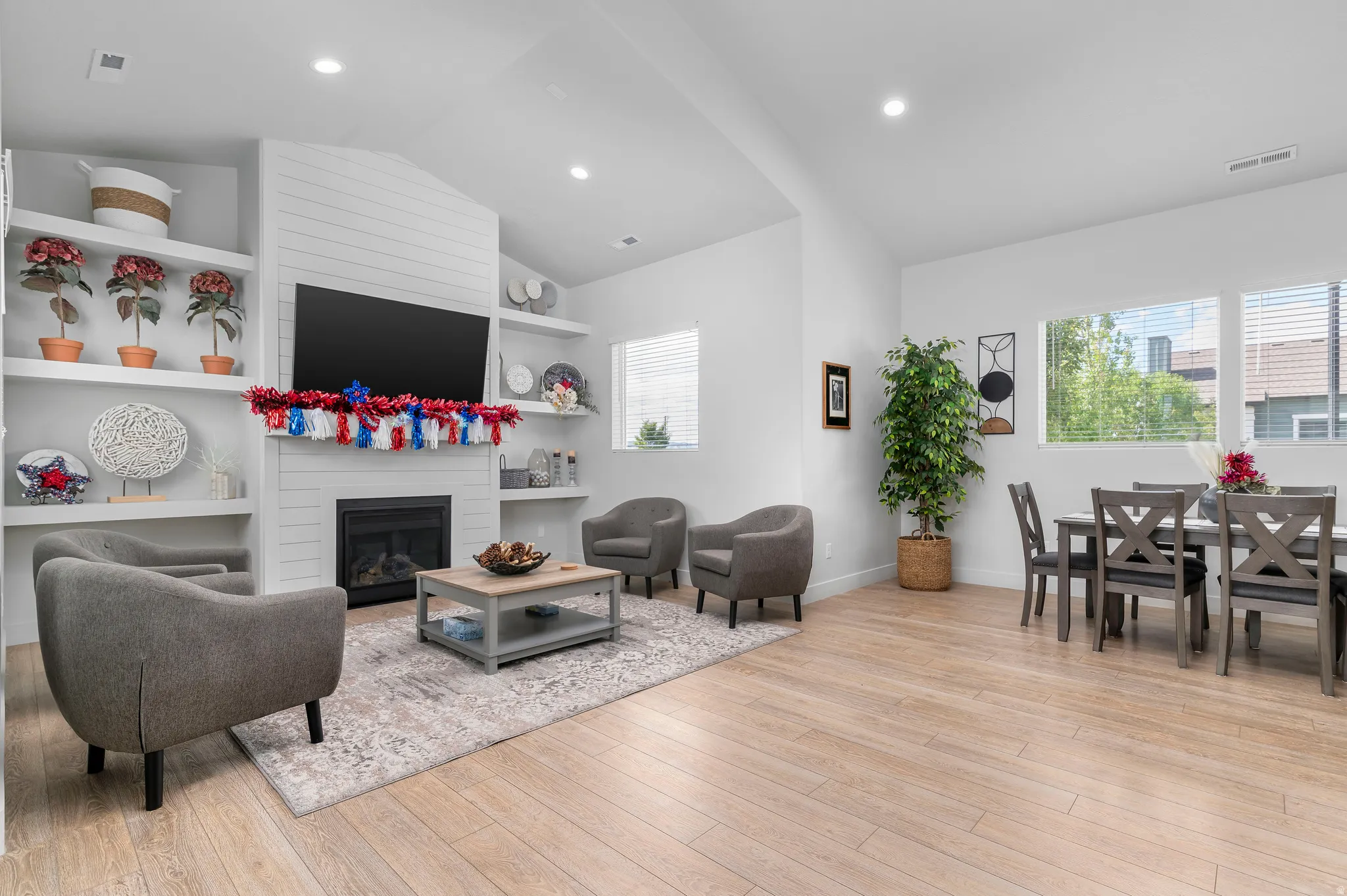 Open-concept living space featuring wood-finish flooring, a contemporary fireplace with horizontal shiplap detailing, and built-in shelving