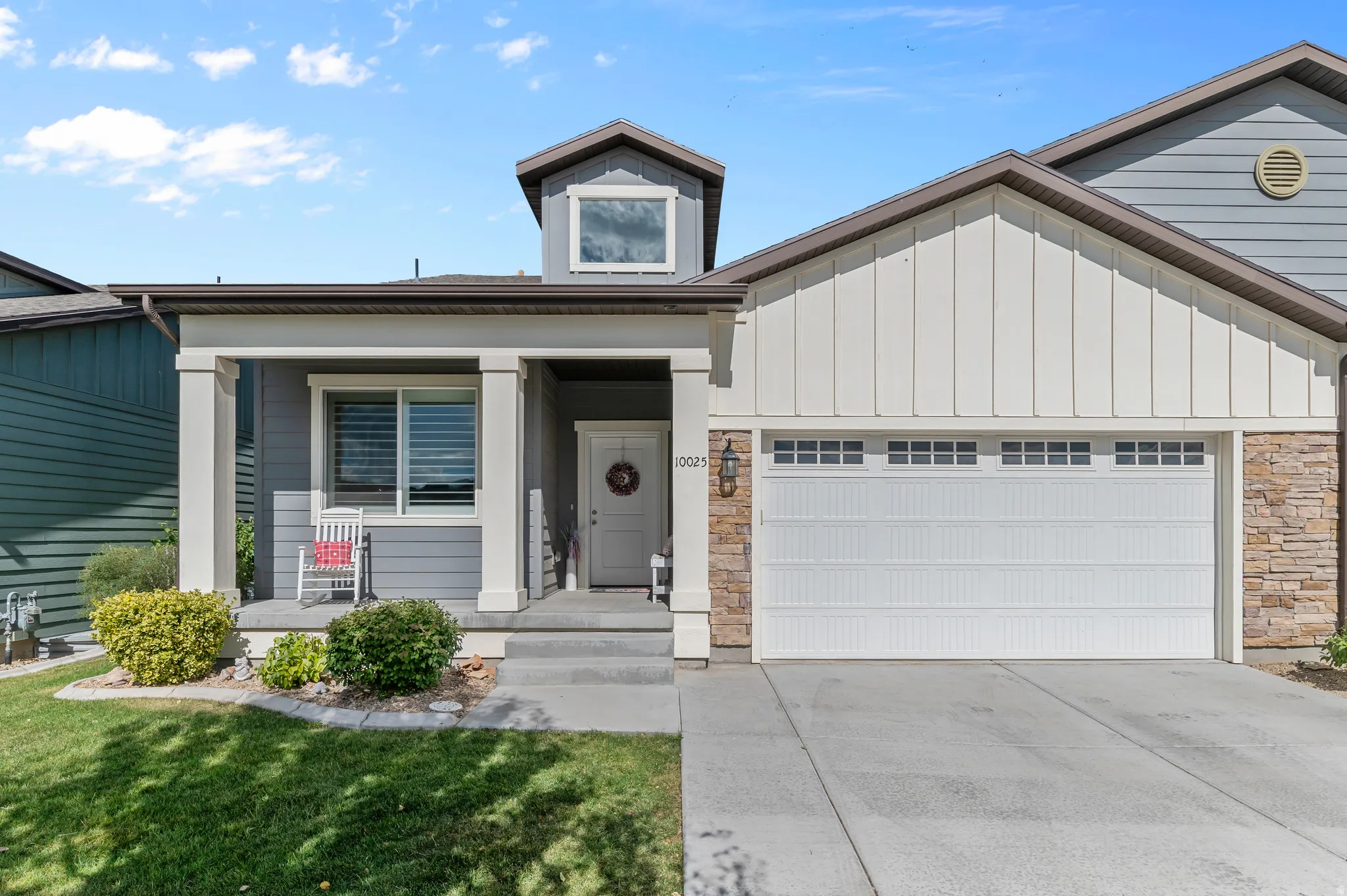 Modern craftsman-style exterior featuring a covered porch with substantial columns, a two-car garage with transom windows, and a stone accent facade