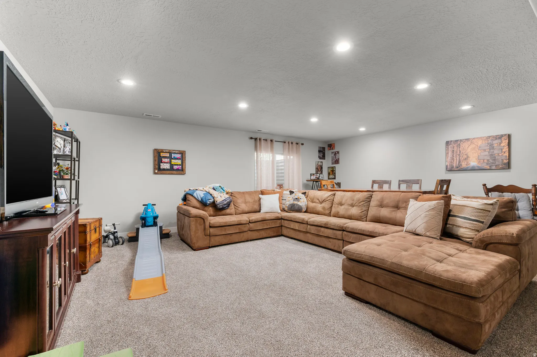 Spacious carpeted room featuring recessed lighting, light gray walls, and a large window with privacy blinds